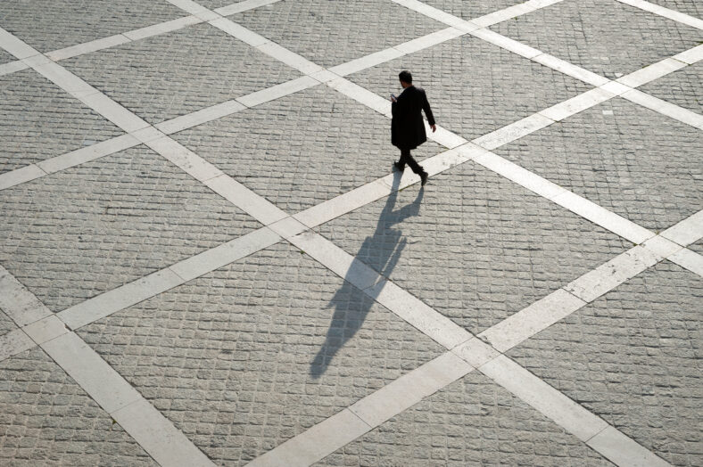 Overhead view of unrecognizable pedestrian casting shadow on the geometric patterns of a stone plaza on a quay next to the River Seine in Paris, France