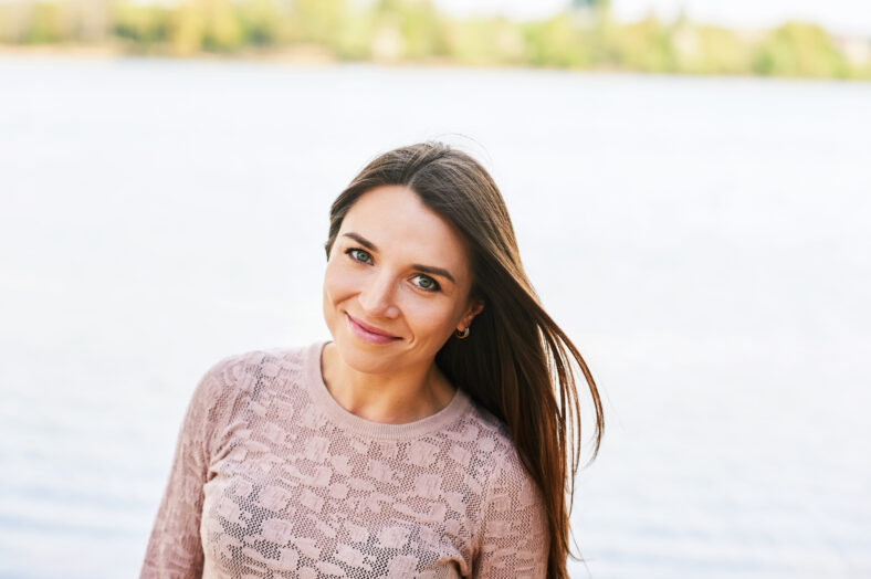 Outdoor portrait of young beautiful woman relaxing by river on a nice warm day