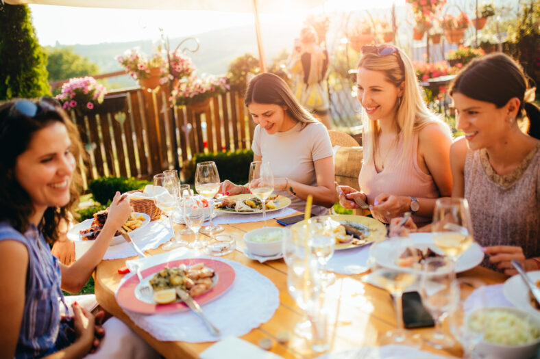 Young beautiful female friends are talking, eating, drinking and smiling while sitting at the table and having lunch
