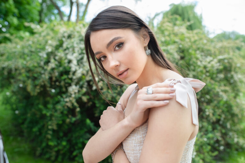 Young beautiful fashionable girl wearing stylish jewelry earrings and ring. Model poses on a street with blooming trees. Spring fashion concept.