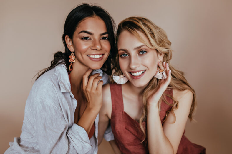 Winsome latin girl posing with best friend. Indoor shot of fashionable blonde woman chilling on beige background.