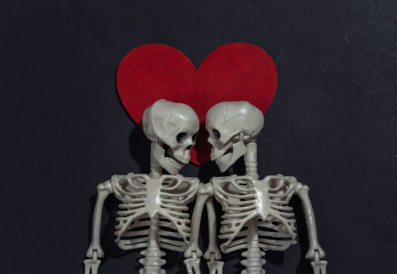 Couple of lovers skeletons and red decorative heart on black background. Valentine's day or halloween theme. Top view. Flat lay