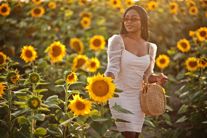 Pretty young black woman wear summer dress pose in a sunflower field.