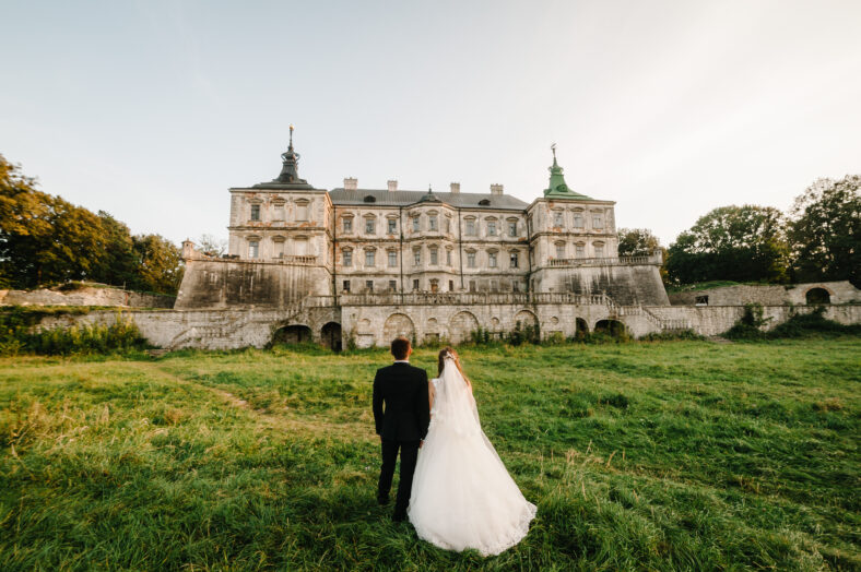 Newlyweds are walking their backs to the vintage Castle, renaissance palace for the wedding ceremony. Photo shoot near Medieval Castle.