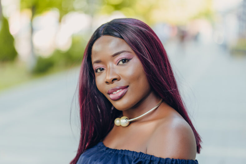 portrait of beautiful young african american woman in blue dress with pink hair hairstyle smiling and walking down the street