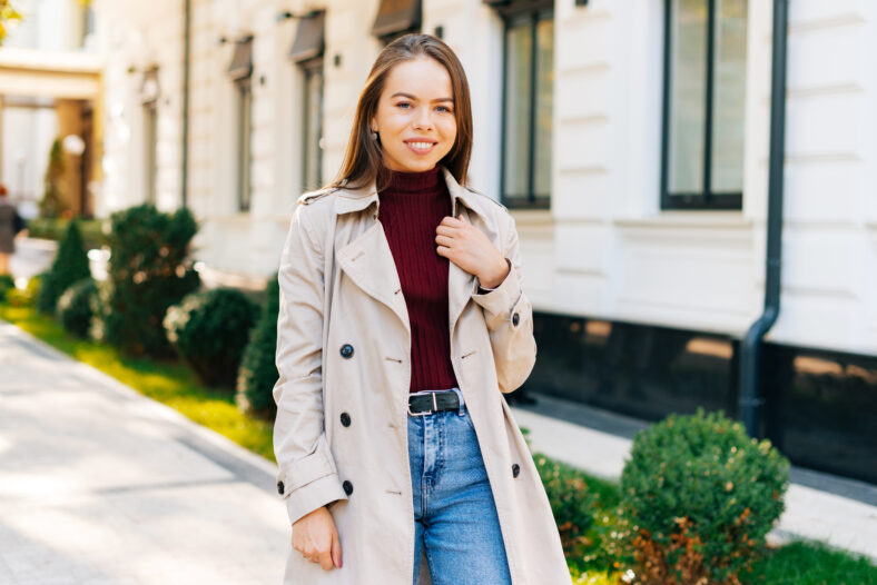 A beautiful young woman is walking and smiling is looking at the camera .