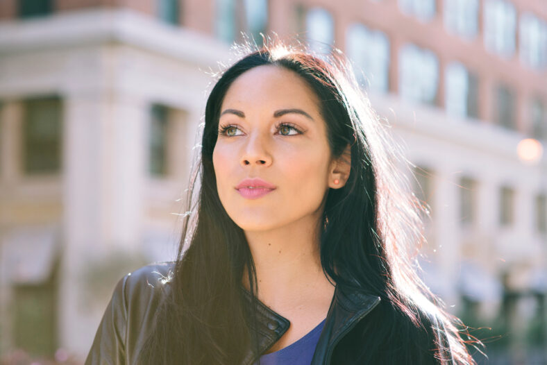 Latina Female stands with strength while looking off to the left - Goal Achievement - Big City - Daytime
