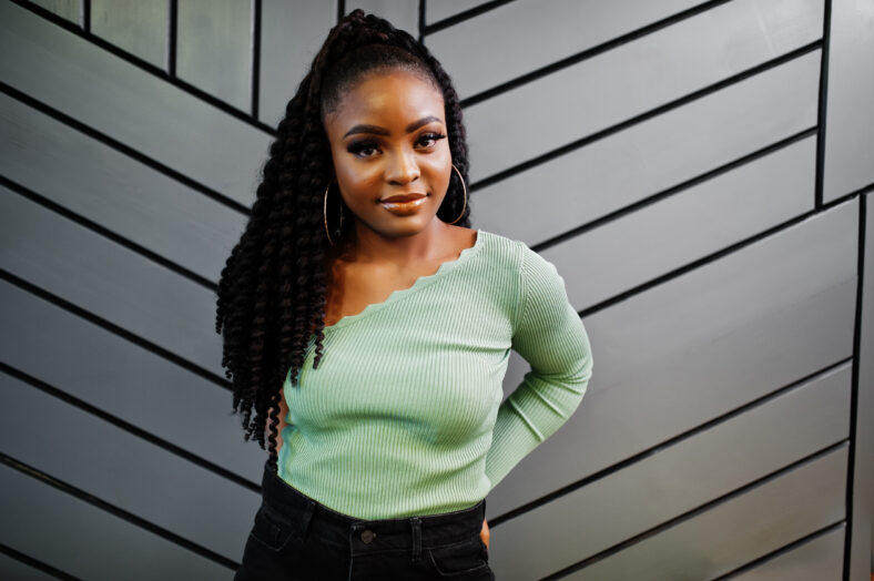 Portrait of attractive young african american woman wearing in green sweater posing against grey wall.