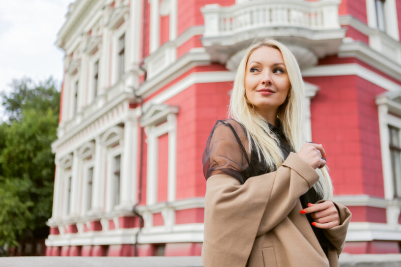 Cute attractive fashion woman in autumn coat posing against the background of urban architecture. Street fashion