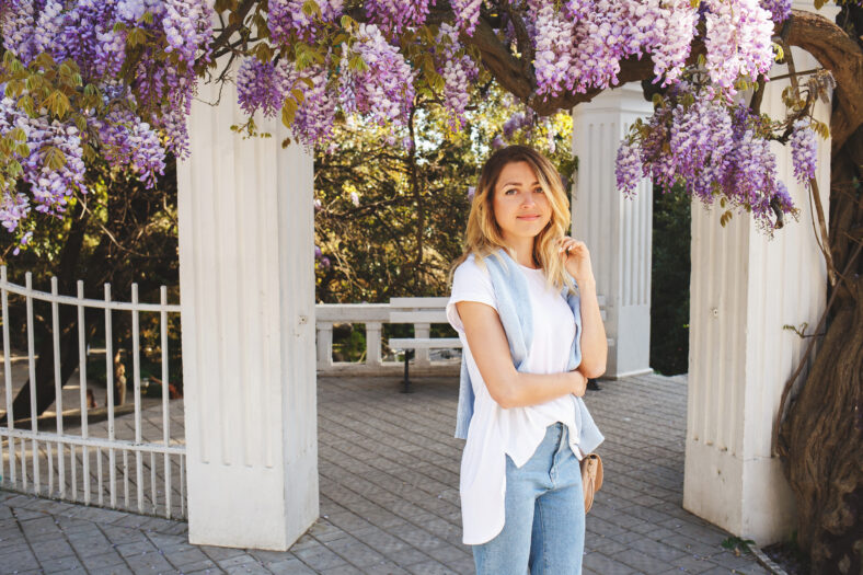 Young beautiful woman in jeans and white t-shirt stands near a flowering Wisteria tree. Spring portrait.