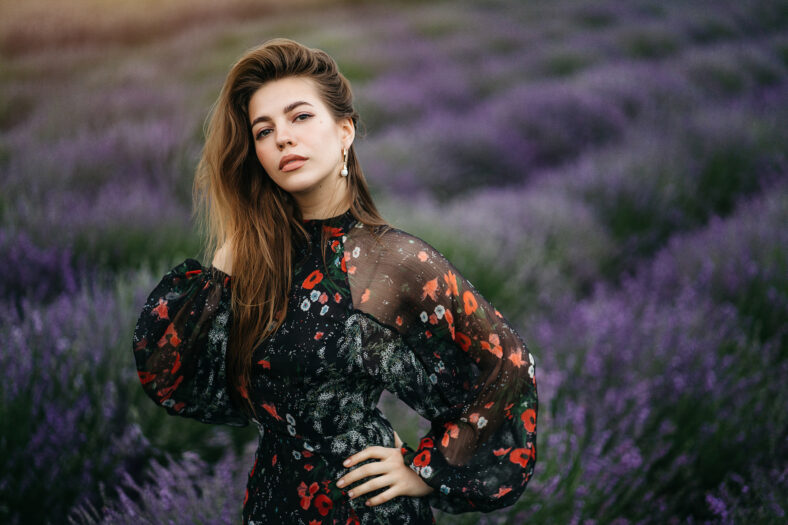 Beautiful young woman portrait in lavender field. An attractive girl with long curly hair in a long dress is dreaming. High quality photo