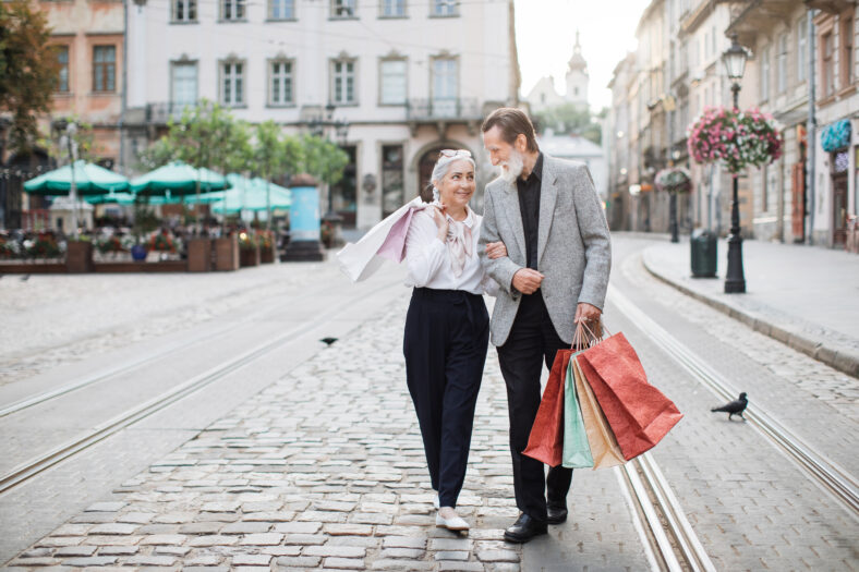 Happy mature family walking in embrace on city street with shopping bags in hands. Lovely couple smiling and looking on each other. Time together.