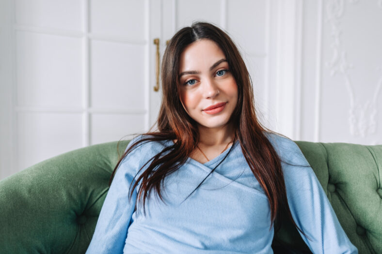 Portrait of attractive pretty young woman in casual clothing sitting on a sofa and looking on camera.
