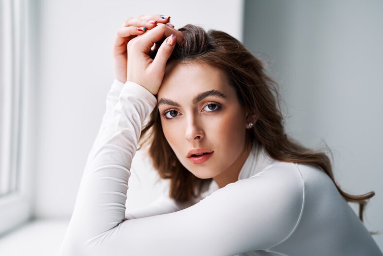 Close up portrait of sensual pretty young woman. Beautiful female model in white cloth with clean skin and sable style eyebrows posing in studio
