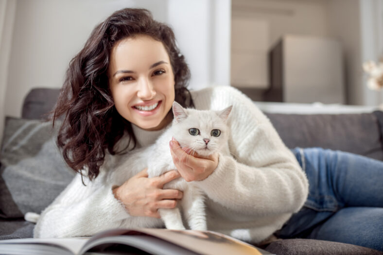 With a cat. Cute woman laying on the sofa and caressing her cute white cat