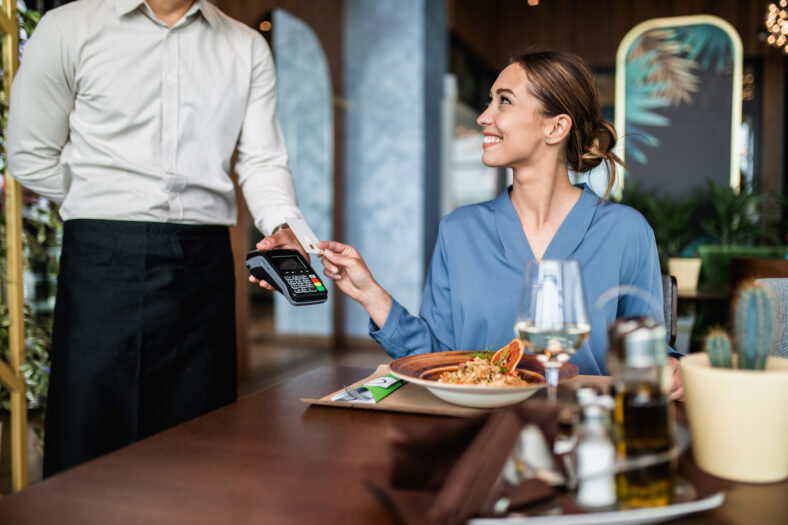 Beautiful young woman paying for her order with a credit card in a restaurant.