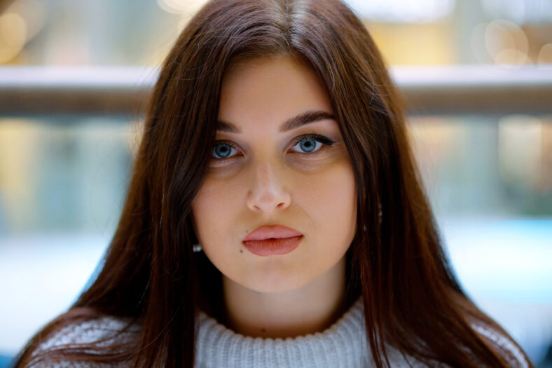 Mujer joven con cabello largo y ojos azules mirando la cámara, fondo borroso. Retrato de primer plano de la hermosa modelo femenina. Concepto de belleza