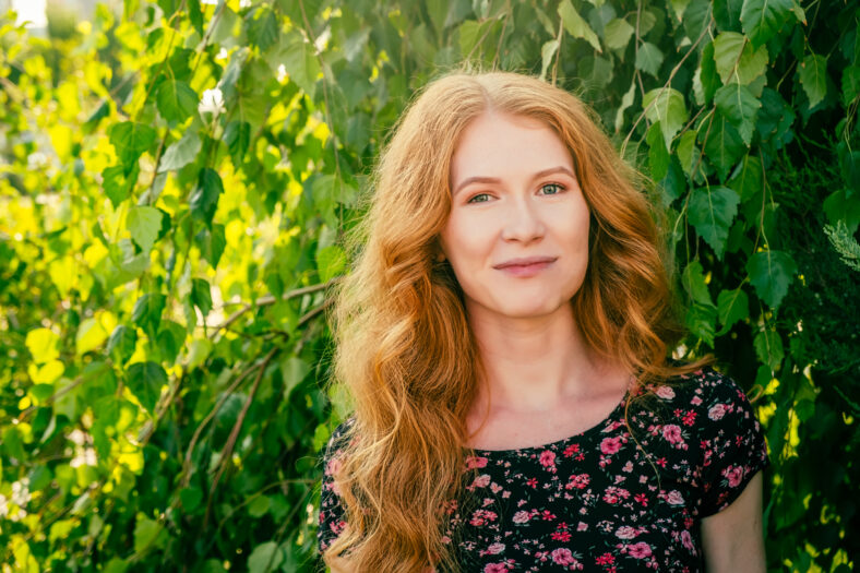 Close-up portrait of lovely lady with long red ginger hair and freckles smiling looking at camera in park in summer. People in nature and happiness concept.