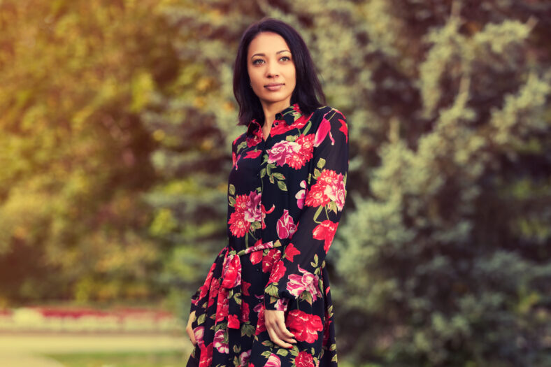 Happy young beautiful woman walking in city park Stylish fashion model with bob hair style in red floral print dress