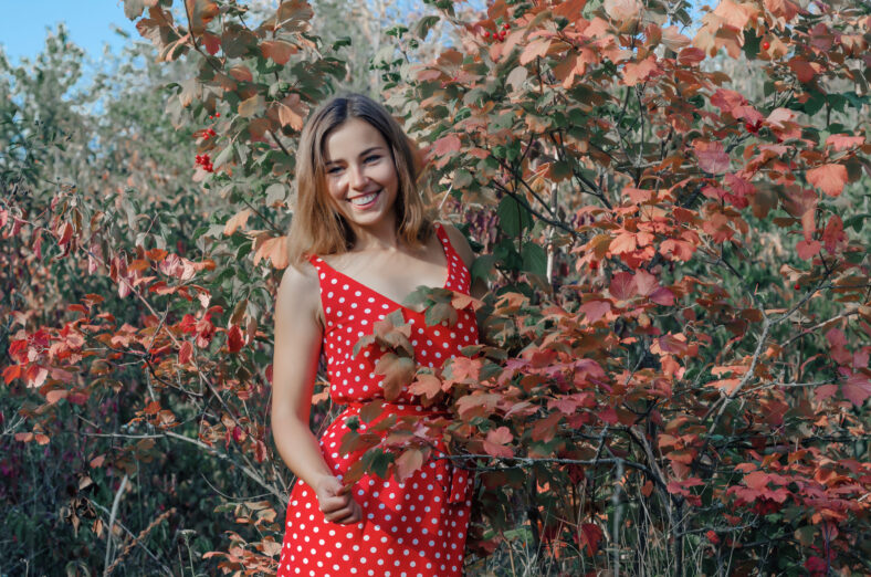 Beautiful girl in a red dress among the woods. Snow-white smile.