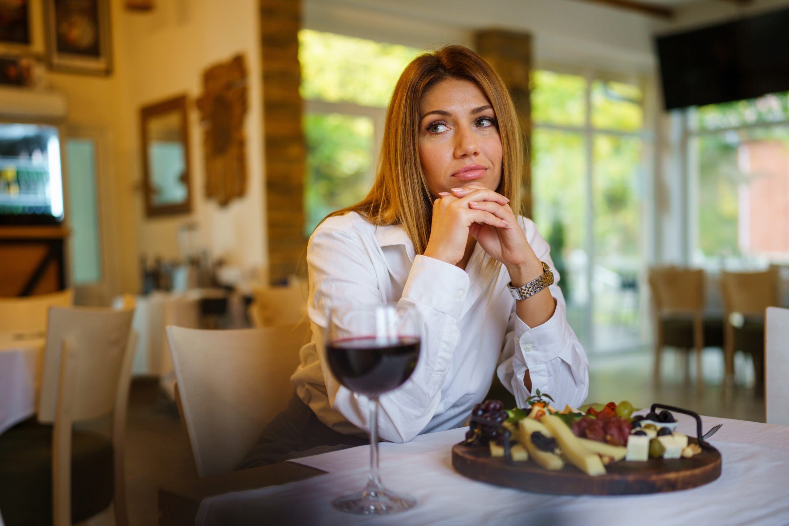 Front view close up portrait of one beautiful caucasian woman sitting alone at the table at restaurant holding head on her hand looking to the side lonely sad at dinner or lunch copy space