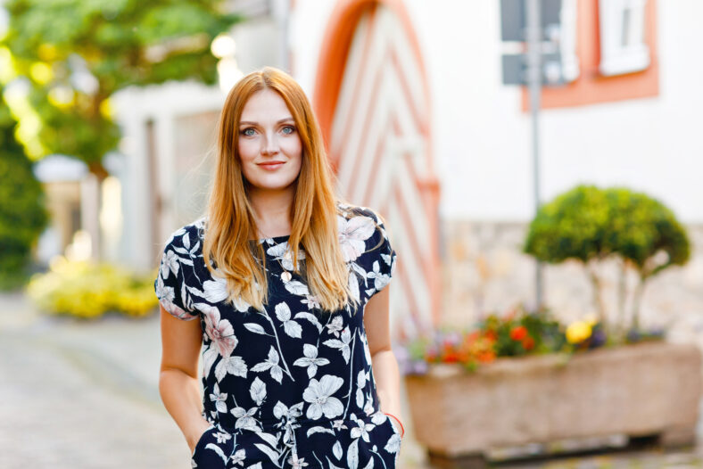 Beautiful young woman with long hairs in summer dress going for a walk in German city. Happy girl enjoying walking in cute small fachwerk town with old houses in Germany