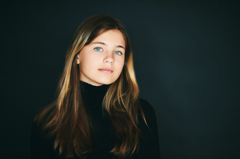 Studio portrait of pretty young teenage girl posing on black background