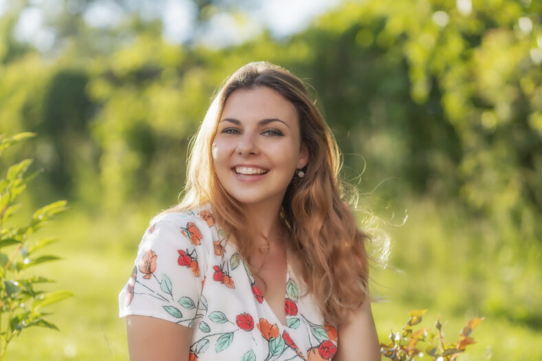 Smiling beautiful young woman is posing outdoors in summer day. Horizontally.