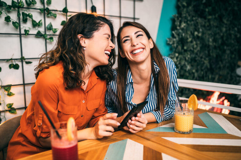 Friends enjoying together in restaurant and looking something at smartphone. They are drinking a fresh beetroot and orange juice.
