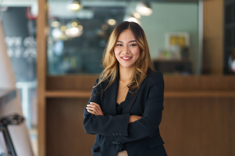 Beautiful young Asian business woman manager smiling looking at camera with crossed arms.