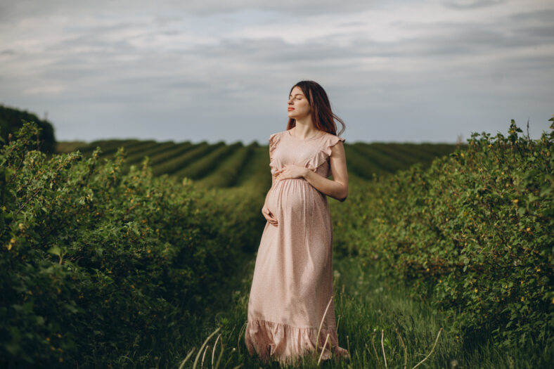 Pretty young pregnant woman in dress relaxing outside in nature at summer day