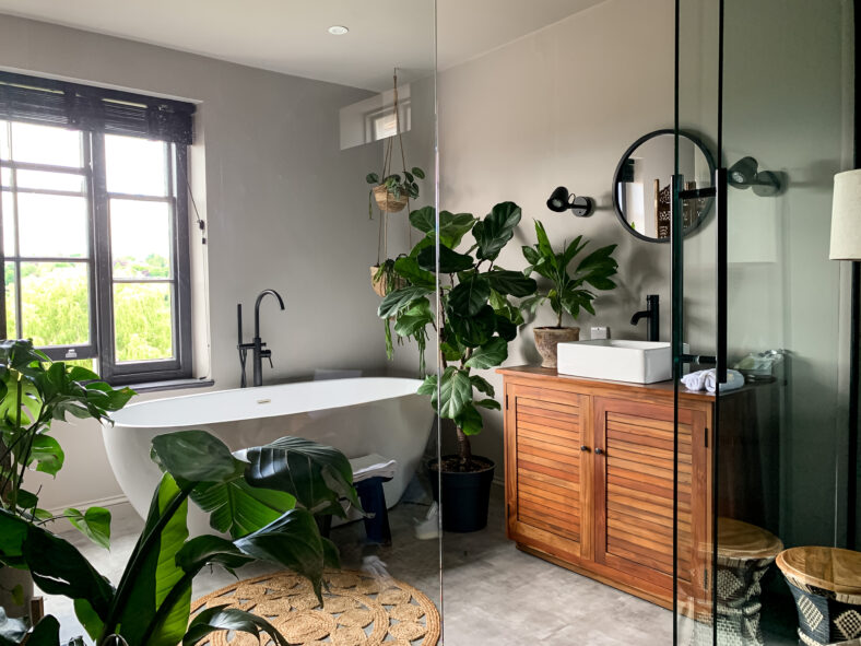 Charming cozy bathroom view. Bath tube by the window. Taking bath at home or in a hotel. Charming cozy indonesian style. Bathroom view. Home Plant in room.