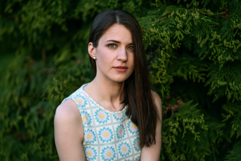 Portrait of a brunette woman in a blue top in the forest in summer. Natural beauty of a lovely girl with long straight brown hair, blue eyes and pale skin.