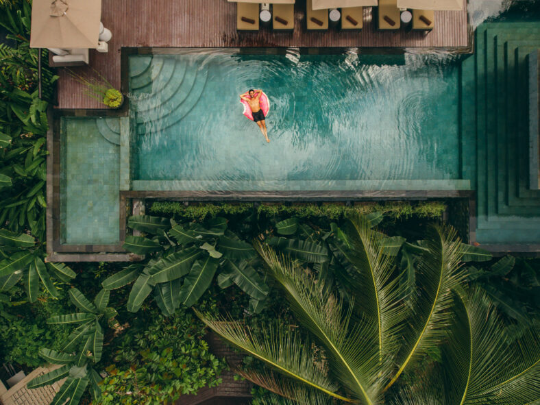 Aerial shot of young man relaxing in resort swimming pool. Male on inflatable ring in pool.