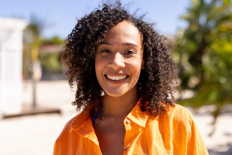 Retrato de feliz mujer afroamericana mirando a la cámara y sonriendo en la playa