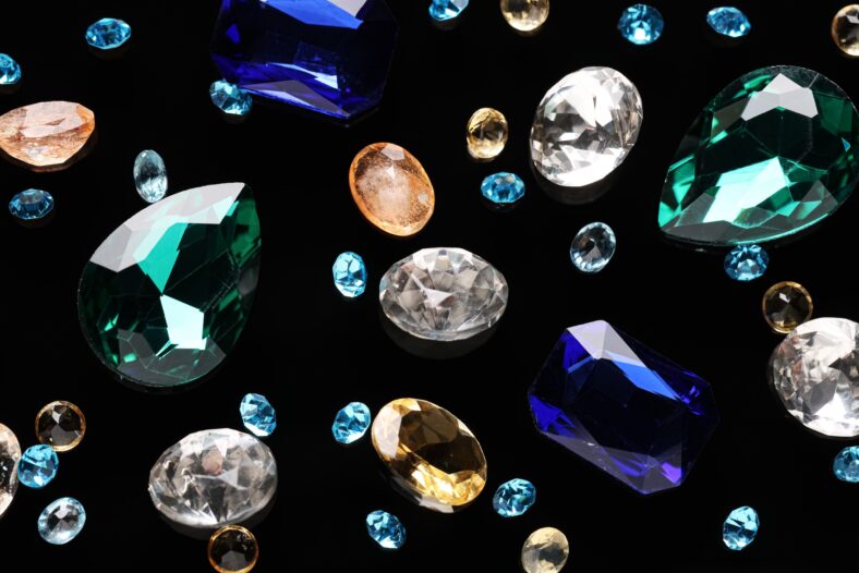 Different beautiful gemstones for jewelry on black background, flat lay