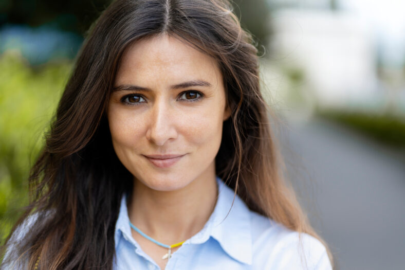 Portrait of beautiful smiling latin woman looking at camera on street. Successful young student posing for picture. Fashion model, stylish female, natural beauty