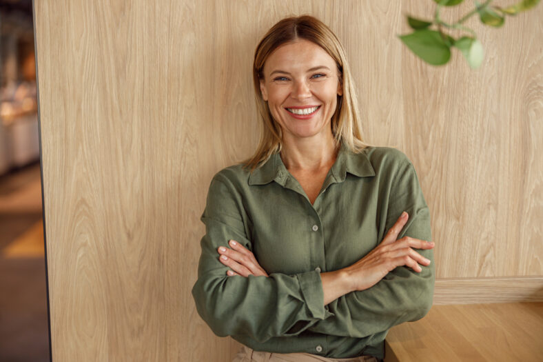 Female entrepreneur standing with crossed hands on coworking space background and looking camera