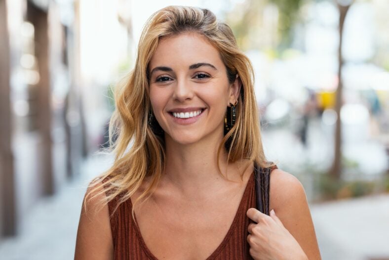 Portrait of beautiful young woman smiling while looking at camera standing in the street.
