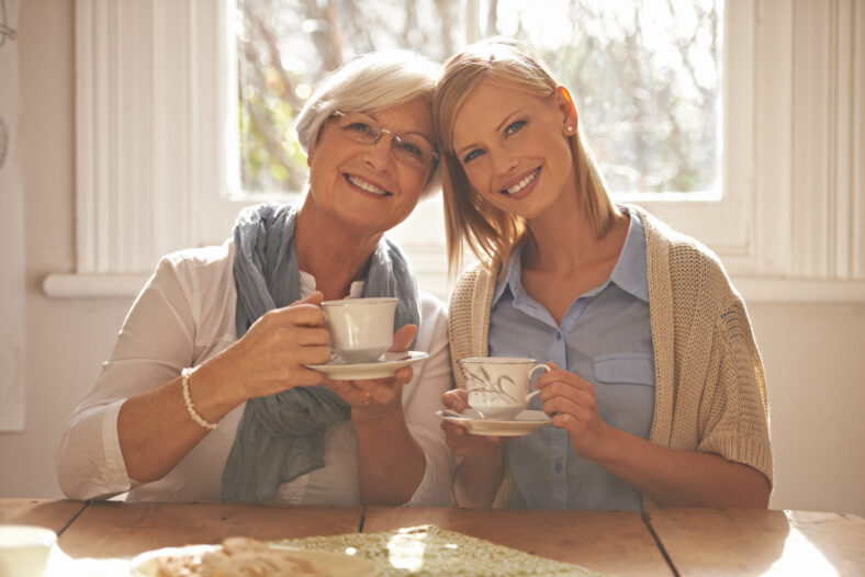 Portrait, happy woman and elderly mother drinking coffee at breakfast in the morning, bonding and smile in house. Face, senior mom and daughter with tea cup at table, love and family at home together.