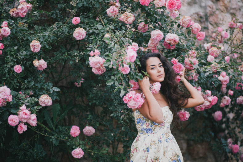Beautiful young woman posing near roses in a garden
