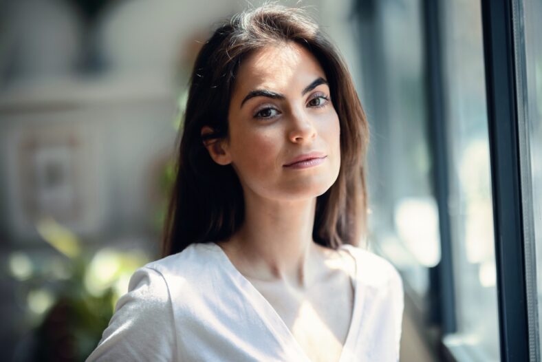 Portrait of smiling young woman posing while looking at camera in the living room at home.