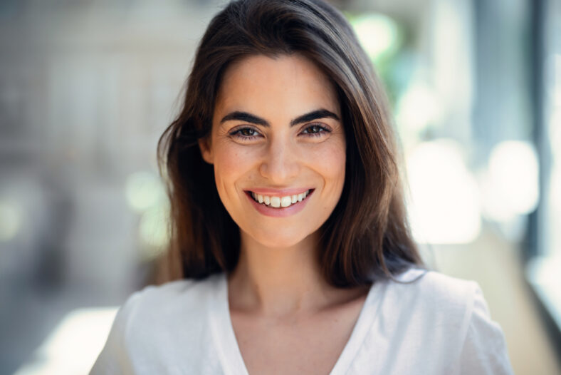 Portrait of smiling young woman posing while looking at camera in the living room at home.