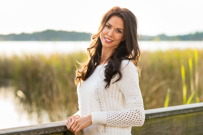 Smiling, pretty brunette on Fall nature walk with tall grass and lake in background