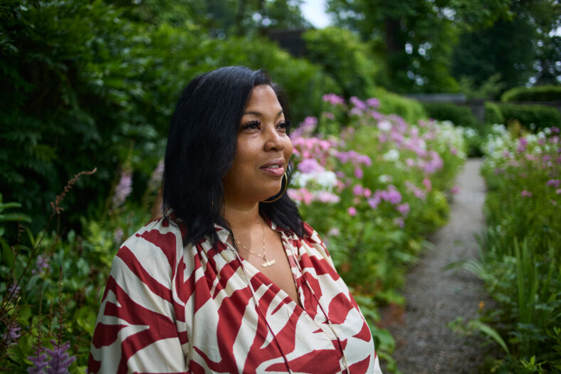 A portrait of a woman on a sunny day in a park surrounded by lush greenery.