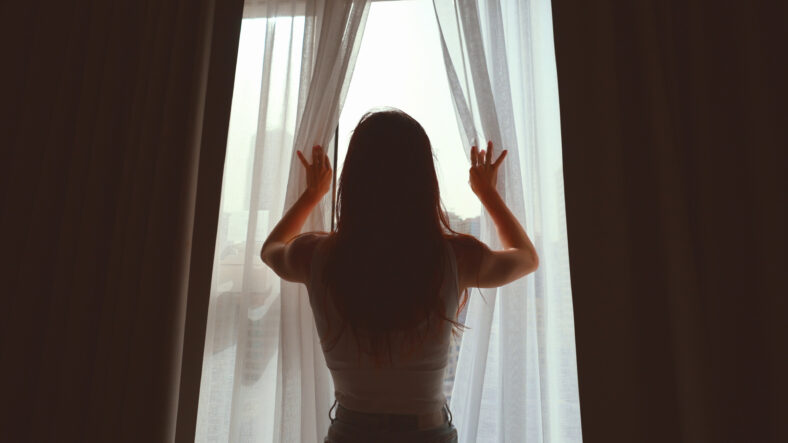 young woman opening curtains in a bedroom