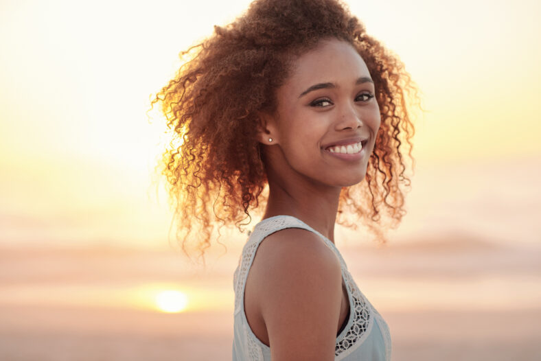 Portrait of a beautiful young woman standing on a beach at sunset