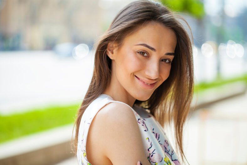 Retrato de cerca de una hermosa joven morena feliz con piel fresca y limpia, calle de verano al aire libre