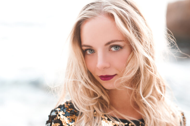 Smiling blonde girl 20-24 year old posing outdoors in sunny light. Looking at camera.
