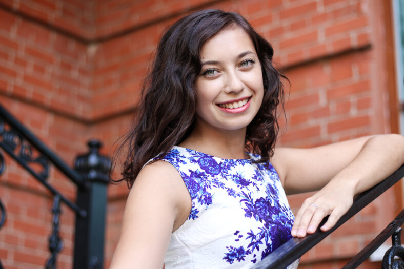 Woman smiling against a backdrop of brick wall holding on to Rails.